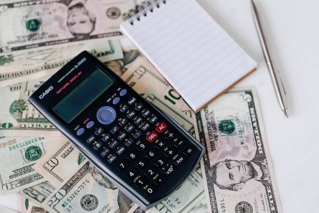 calculator, pen and notepad on a pile of USD bills